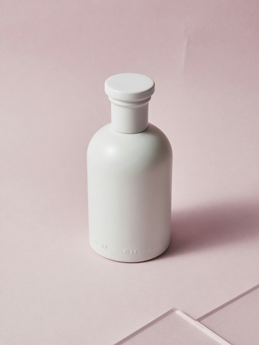 White ceramic perfume bottle against a pink studio background